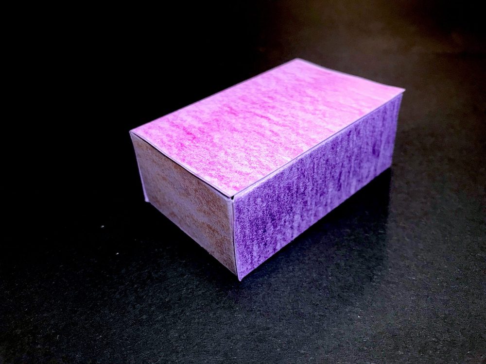 Foto eines aus Papier gebastelten, rosa-violett ausgemalten Quaders als Ergebnis einer echten praktischen Leistungserhebung in Geometrie.